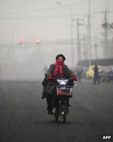 A resident wearing a scarf over her mouth rides a bicycle in Beijing on 5 December 2011