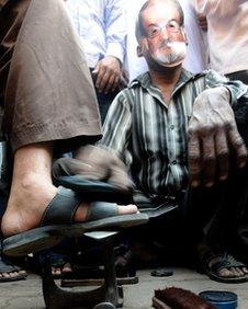 A cobbler wearing a Salman Rushdie mask polishes shoes outside a mosque during a protest by an Islamic organisation in Mumbai on January 11, 2011.