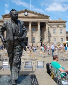 A statue of Harold Wilson in front of Huddersfield's railway station, a listed building