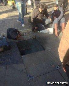 The woman lies injured as smoke emerges from the manhole
