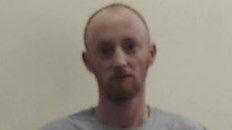 A poor quality police custody picture of Christopher Brown, who has short ginger hair and is wearing a grey top.