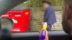 Still of a man in a car spraying a water pistol at a boy walking past who wears an Orthodox Jewish hat.