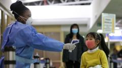 A Kenyan health worker (L) screens a passenger wearing face mask after they arrived from China, at Jomo Kenyatta International Airport in Nairobi, Kenya, 29 January 2020