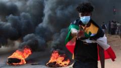 A Sudanese protester draped with the national flag flashes the victory sign next to burning tyres during a demonstration in the capital Khartoum, on October 25, 2021