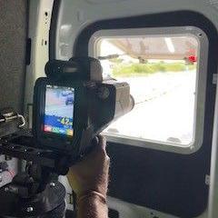 A colour speed camera points through the back window of a van.