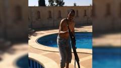 Choukri Ellekhlif posando à beira de uma piscina com uma arma nas filmagens do smartphone