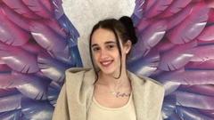 Joana stood against a wall with multi-coloured rainbow wings painted on