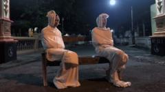 Two volunteers sit dressed as traditional pocong on a bench