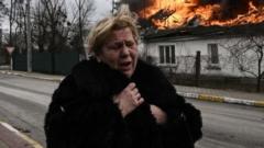 A woman stands in front of a house burning after being shelled in the city of Irpin, outside Kyiv, in March 2022