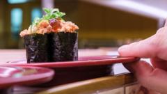 A hand takes a sushi roll plate off a conveyor belt at a restaurant