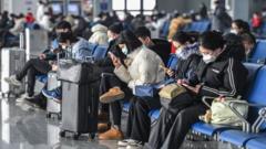 Passengers wearing masks check their mobile phones in the waiting room of a train station in China