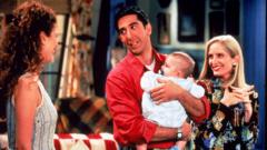 American actor David Schwimmer holds a baby, as actors Jessica Hecht (L) and Jane Sibbett look on, in a still from the television series, 'Friends in 1995