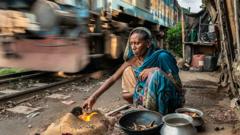A woman cooks a meal over a fire as a train hurtles by behind her