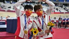 钟天使（右）、鲍珊菊（左）接受奥运金牌后朝着摄影记者做出心形姿势（2/8/2021）