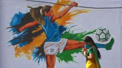 महिला फुटबॉलरच्या भित्तीचित्रासमोरून जाणारी महिला. एएफसी विमेन्स एशियन कपच्या निमित्तानं नवी मुंबईत हे चित्र रंगवलं होतं.