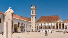 Torre da Universidade de Coimbra diante de pátio com pessoas caminhando em um dia de sol; há uma estátua de costas