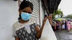 A woman displays a food bag while standing near to the people waiting in queue outside a state-run supermarket to buy essential food items in Colombo on September 3, 2021 as Sri Lanka began imposing price controls on essential food from September 3 after using a state of emergency to seize allegedly hoarded stocks of sugar and rice.