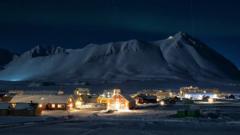 Tiny settlement of town of Ny-Ålesund, - with lights on as darkness falls over mountains in background
