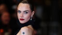 Cara Delevingne has dark hair scraped back into an up-do. She has red lipstick on and is wearing a dress with a black halterneck and open back.