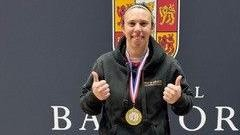 A fair-haired woman in a black hoodie wears a gold medal with her thumbs up.