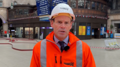 Network Rail Scotland's route director Ross Moran, wearing a white hard hat and and orange hi-vis jacket stands on the concourse of Glasgow Central station with fire hoses lying on the floor and tape cordons behind him.