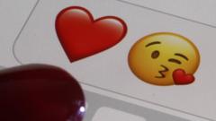 photo illustration, emoji or emoticon representing a heart and a kiss are displayed on the screen of an iPhone