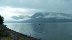 A stunning landscape of a Scottish loch, calm and empty, save a lone small fishing boat. Mountains frame the background and mist weaves its way up and down the outline of the hills