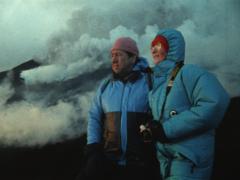 Maurice e Katia aparecem lado a lado, com jaqueta azul, observando vulcão