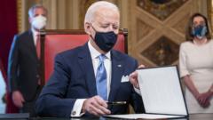 O presidente dos EUA, Joe Biden, de máscara, segura uma caneta em frente a uma pasta com um documento; ele estava assinando o documento oficial de posse como presidente