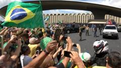 Dezenas de pessoas tiram fotos, levantam cartazes e bandeiras diante de Bolsonaro, que acena de cima de carro em área externa de Brasília