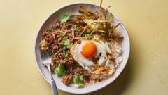 A bowl filled with braised beef mince and rice, topped with a fried egg on a yellow surface