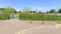 The school seen from the road outside - you can mostly just see a hedge and the green school gates.