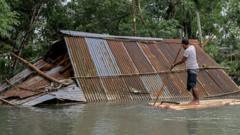 Homem navega perto de casa submersa pela água de enchente em Bangladesh