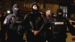 Andrew Tate (hooded) and Tristan Tate are escorted by police officers outside the headquarters of the Directorate for Investigating Organized Crime and Terrorism in Bucharest (DIICOT)