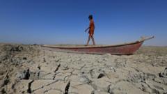 伊拉克濟加爾省奇巴伊什縣一位男孩站在擱淺乾涸濕地上的小船上（28/6/2022）