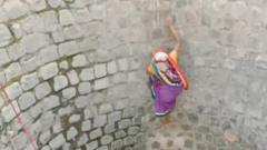A still from the video showing woman scaling the wall of a well without any support