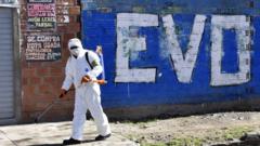 Trabajador de limpieza desinfectando una calle delante de una pinta de Evo Morales.