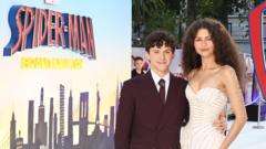 Tom Holland and Zendaya promoting Spider-Man: Brand New Day at Wednesday's London premiere. He has a dark suit on while she is wearing a white dress. He has his arm around her waist and they are both stood in front of a film poster.