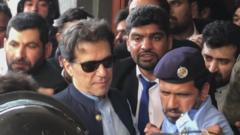 Imran Khan leaving court on Friday. He is wearing sunglasses and making his way through a crowd of people.