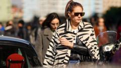 A guest wears earrings, sunglasses, a beige and black zebra pattern jacket, a black leather jacket, outside MSGM, during Milan Fashion Week Fall/Winter 2020-2021 on February 22, 2020