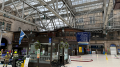 two firefighters standing inside Glasgow's central station. part of the station is cordoned off an a large hose is visible.