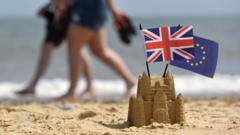 A couple walk on a beach behind a sandcastle with EU and UK flags