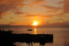 An orange sunset over a harbour, with sailing boats in the water.
