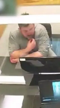 McCullagh in a grey tshirt behind a glass screen looking at a TV screen.