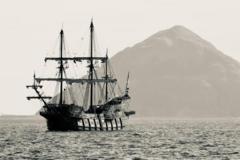 A replica galleon with tall masts at sea, with a large island in the background.