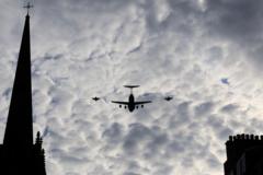 Three military aircraft silhouetted in a cloudy sky, alongside a steeple and chimneys.