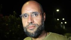 Saif al-Islam Gaddafi appears in front of supporters and journalists at his father's residential complex in Tripoli in 2011.