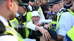 Police officers surround and arrest an old woman who appears to be in distress as they lift her off the ground.