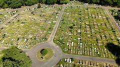 An aerial shot of a cemetery with wide pathways, graves on each side, and a traffic roundabout