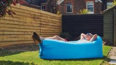 Homem de óculos escuros, bermuda e camiseta deitado em sofá inflável tomando sol no jardim de casa